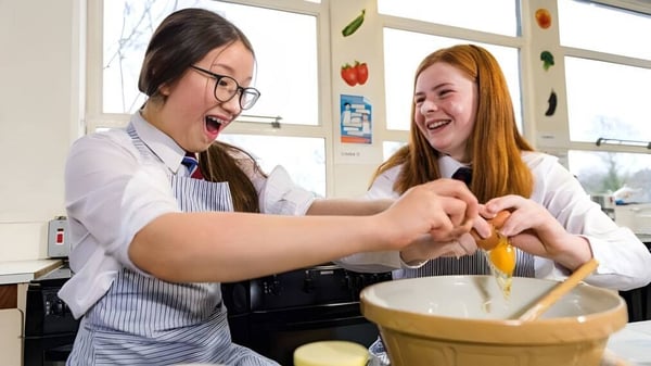 Dos estudiantes del Victoria College Belfast están trabajando juntas y riendo en una cocina escolar.