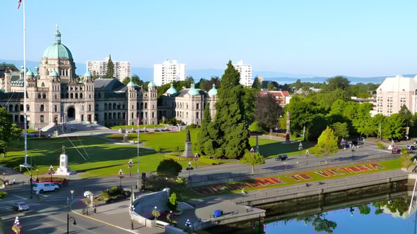 Un edificio gubernamental histórico con techo verde cerca de Victoria High School está rodeado de áreas verdes y un canal.