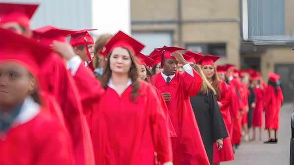 Un grupo de graduados de Victoria High School está en togas rojas frente a un edificio escolar.