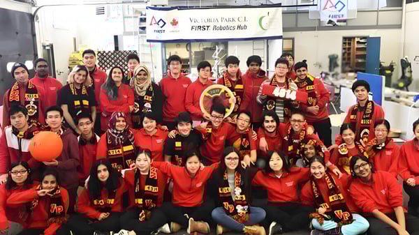 Un gran grupo de estudiantes del Victoria Park Collegiate Institute posan con chaquetas deportivas rojas en un gimnasio.