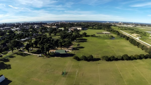 Un gran campo verde con árboles dispersos frente a un horizonte urbano se puede ver cerca de la Victoria Park High School.