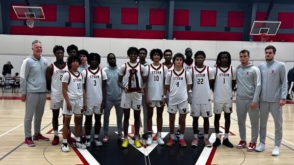 Un grupo de jugadores de baloncesto posan en la cancha de baloncesto de la Victory Christian Academy frente a paredes rojas y blancas.