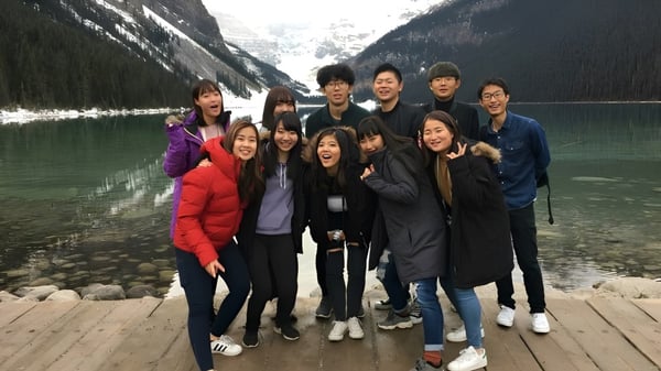 Un grupo de personas está en la Viking School en un muelle de madera frente a un paisaje montañoso con lago.