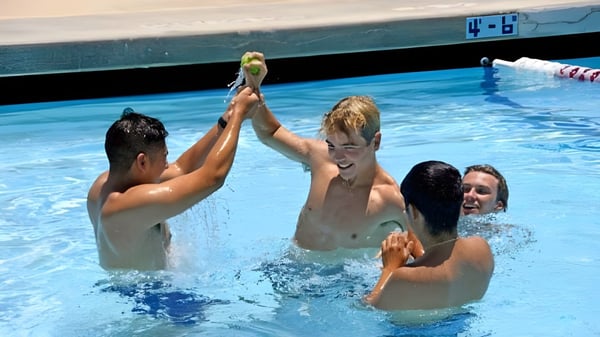 Estudiantes de la Villanova Preparatory School chapotean y juegan en la piscina con un tablero de puntuación al fondo.