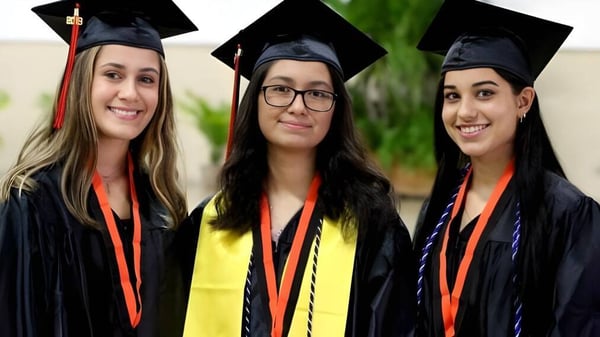 Tres estudiantes de la Vineridge Academy posan con ropa de graduación frente a un fondo verde.