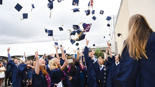 Los graduados con togas azules de la Vistamar School lanzan sus sombreros al aire durante la ceremonia de graduación.