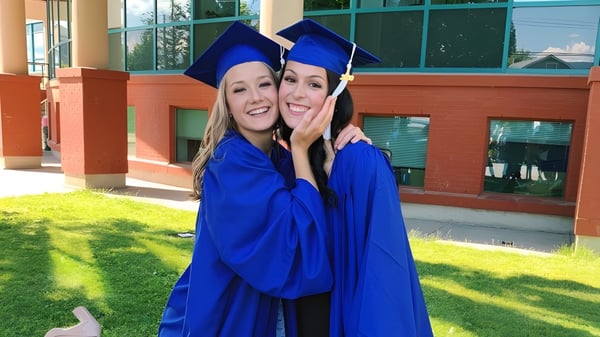 Dos alumnas sonrientes en togas de graduación azules están frente al edificio de W. L. Seaton Secondary School.