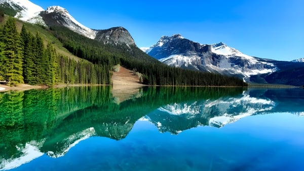 Un tranquilo lago alpino con montañas nevadas y un bosque verde se refleja en el terreno de W. L. Seaton Secondary School.