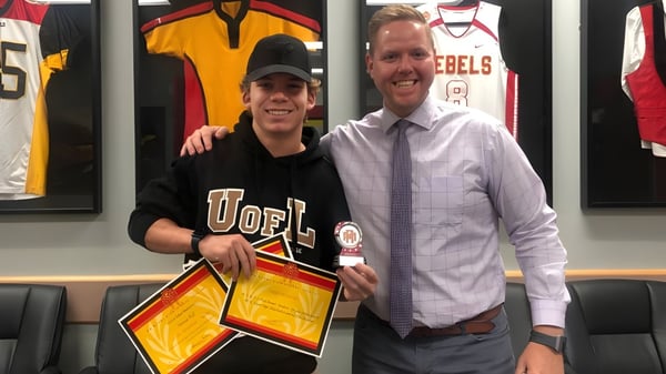 Un hombre y una mujer están en un entorno deportivo con camisetas deportivas de fondo en el campus de la W.R Myers High School.