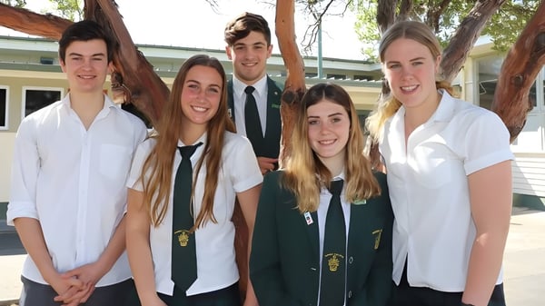 Un grupo de cinco alumnas y alumnos está de pie frente a un edificio en el campus del Waimea College.