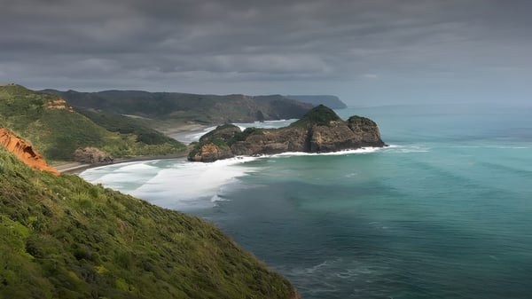 Paisaje costero rocoso con agua turquesa y densa vegetación cerca de Waitakere College.