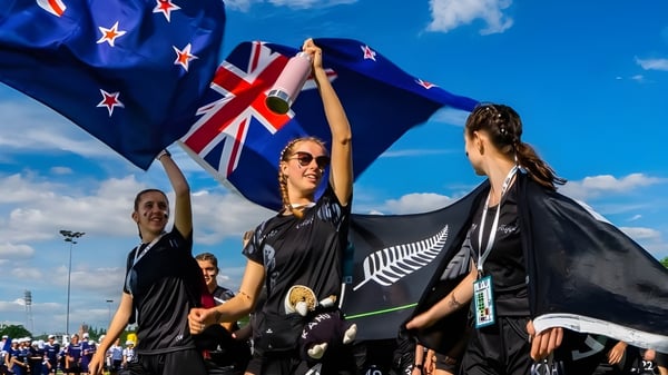 Un grupo de alumnas y alumnos de Waitakere College agita la bandera neozelandesa bajo un cielo azul con la bandera del Reino Unido y la bandera del helecho plateado.