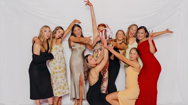 Un grupo de estudiantes de la Waitaki Girls’ High School posan con vestidos coloridos frente a un fondo blanco en un estudio.