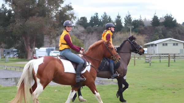 Dos personas montan caballos en un campo cubierto de hierba en el campus del Waiuku College.
