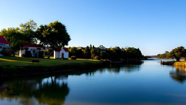 Un tranquilo camino de agua con edificios coloridos y árboles se refleja en el agua en el terreno del Waiuku College.