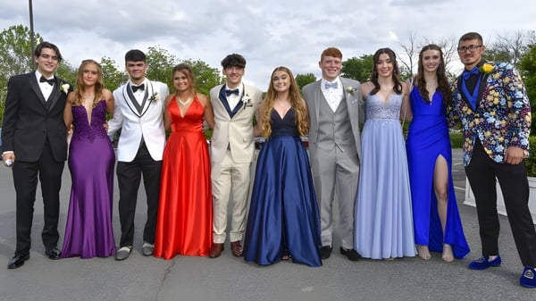 Un grupo de estudiantes de Wakatipu High School posan con ropa formal al aire libre frente a árboles y un cielo nublado.