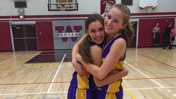 Dos estudiantes de la Wallaceburg District High School se abrazan y sonríen en la cancha de baloncesto frente a un cartel de Tartans.