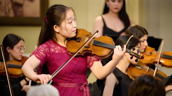 Una estudiante de la Walnut Hill School for the Arts toca el violín en el escenario junto a otros músicos.