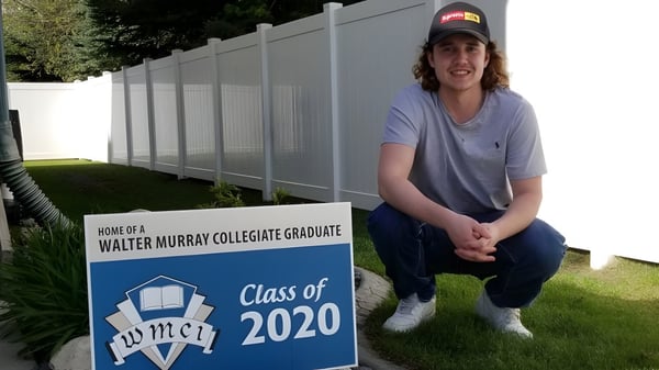 Un estudiante está sentado junto a un cartel de la Walter Murray Collegiate Graduate Class of 2020.