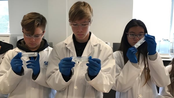 Tres personas con batas de laboratorio blancas trabajan en un laboratorio en la Walter Murray Collegiate.