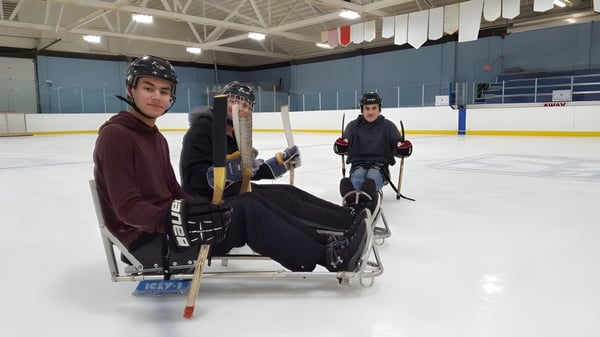 Tres estudiantes de la Warburg School en equipo de hockey sobre hielo están sentados en un banco en la pista de hielo.