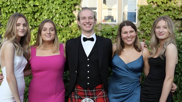 Un grupo de cinco personas está vestido formalmente frente a una pared cubierta de vegetación en el terreno de Warminster School.