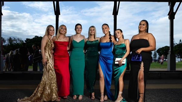 Seis alumnas de la Warners Bay High School están en vestidos de noche frente a un paisaje con cielo nublado.