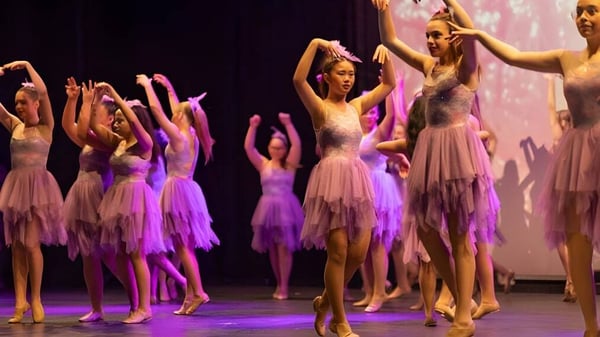 Las estudiantes realizan una presentación de baile con trajes rosa-lila en el escenario de Warwick Senior High School.
