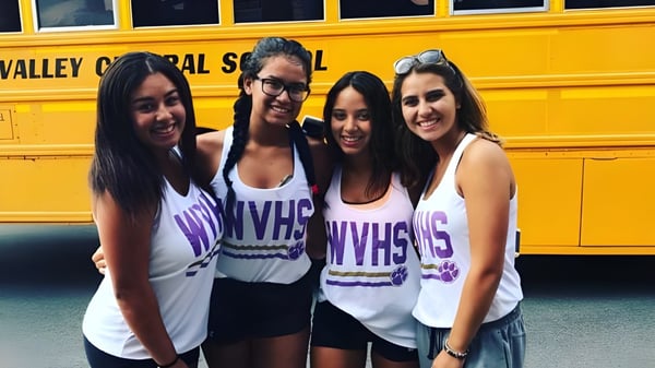 Cuatro estudiantes de la Warwick Valley High School posan frente a un autobús escolar amarillo.