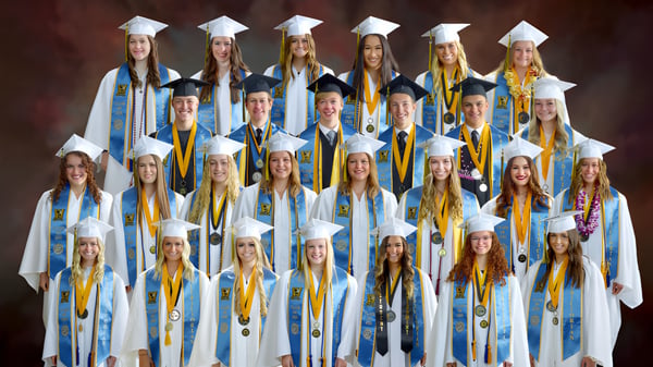 Un grupo de graduados de la Wasatch Academy en togas azules y amarillas frente a un fondo rojo.