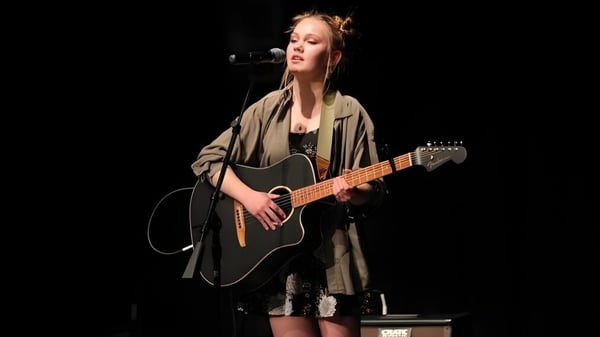Una estudiante de la Wasatch Academy toca la guitarra acústica en el escenario y canta en un micrófono.