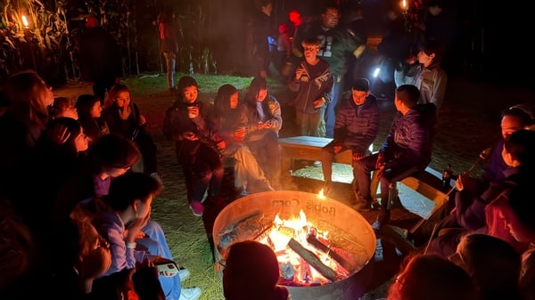 Un grupo de estudiantes de la Washington Preparatory School está sentado al aire libre alrededor de una fogata y conversando.