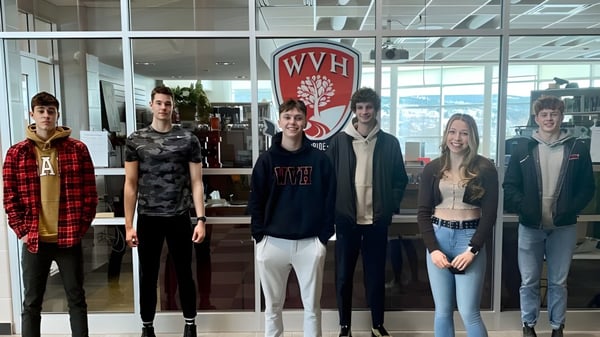 Un grupo de estudiantes está frente al gran logo de WVH en el edificio de la Waterford Valley High School.