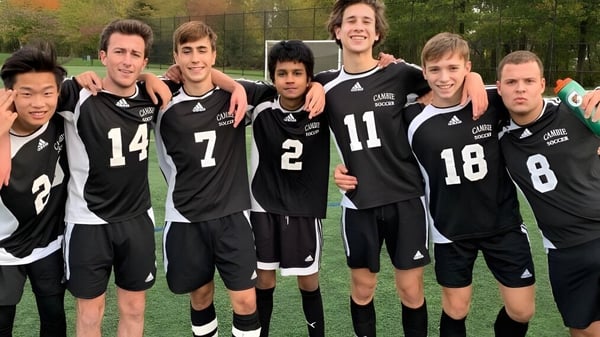 Un grupo de estudiantes del Waterloo Catholic District School Board está en un campo deportivo rodeado de árboles.
