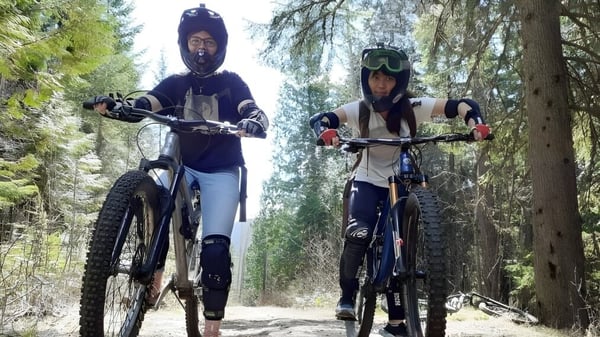 Dos personas del Waterloo Region District School Board montan en bicicleta de montaña con ropa de protección en un sendero forestal.