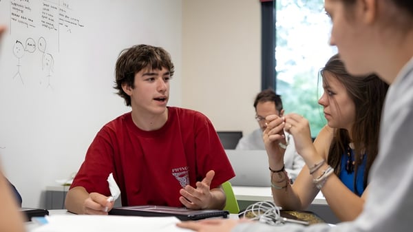 Un estudiante del Wellington College discute en el aula con otras dos personas frente a un pizarrón.