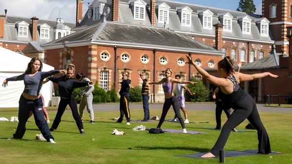 Estudiantes del Wellington College practican yoga en un campo de césped frente a un edificio histórico de ladrillo.