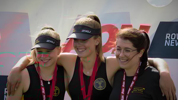 Tres estudiantes del Wellington Girls' College posan juntas frente a un fondo colorido.