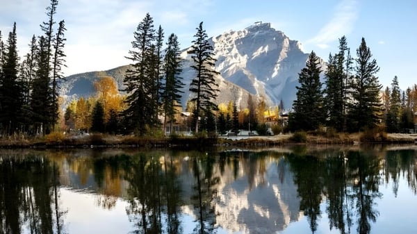 Un tranquilo lago de montaña con pinos circundantes y un pico cubierto de nieve reflejándose en el agua.