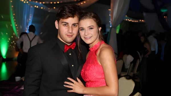 Una joven pareja se abraza en un evento festivo de la Wellington School con luces de colores de fondo.