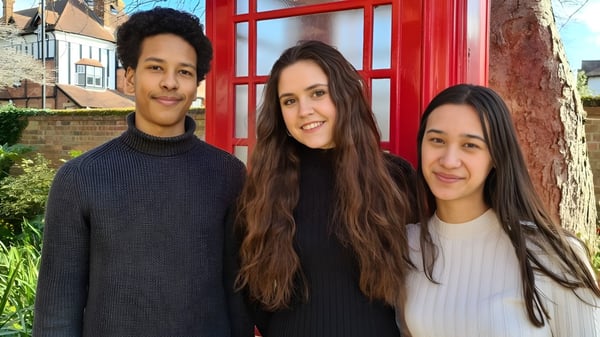 Tres jóvenes están frente a una cabina telefónica roja en el terreno de la Wells Cathedral School.
