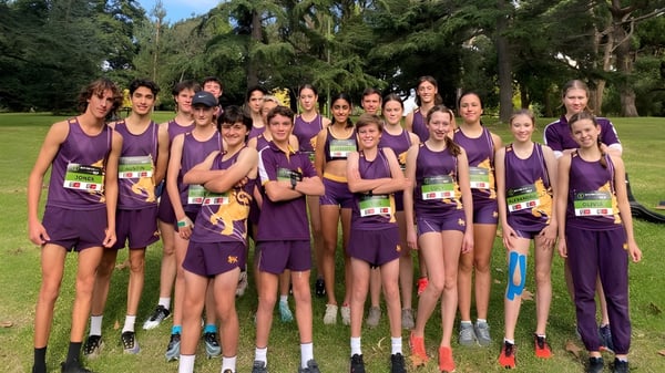 Un grupo de jóvenes atletas en uniformes morados está de pie en un campo en el campus del Wesley College.