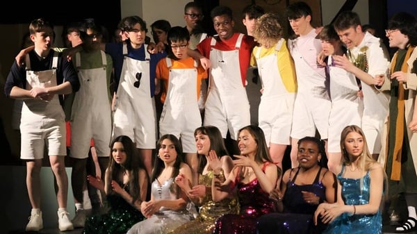 Un grupo de estudiantes está en el escenario del Wesley College y se presenta con trajes coloridos.