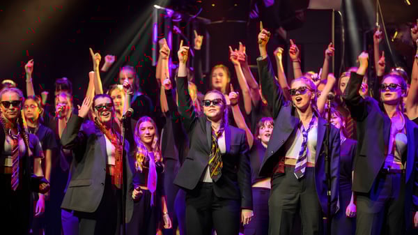 Un grupo de estudiantes de la West Buckland School está en el escenario con los brazos en alto bajo luces de colores.