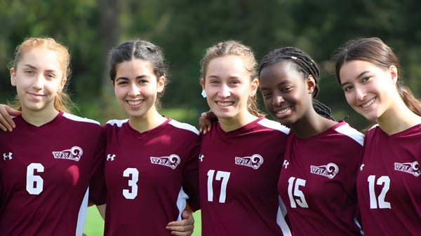 Un grupo de cinco estudiantes de la West Nottingham Academy está juntos al aire libre en un prado con árboles de fondo.