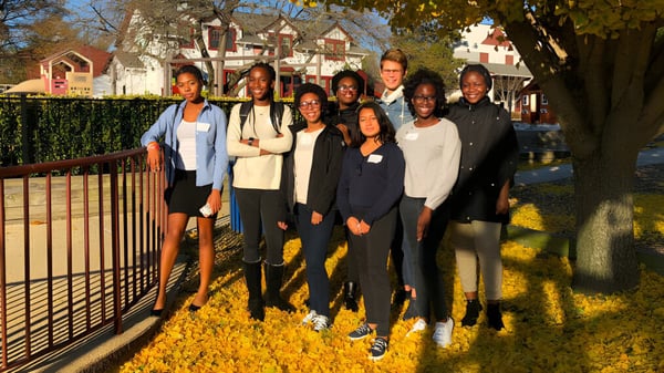 Un grupo de estudiantes y adultos está al aire libre frente a un colorido follaje otoñal en el terreno de la West Nottingham Academy.