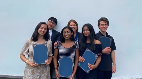 Un grupo de estudiantes de la Westbourne School está frente a un fondo azul claro y sostiene carpetas azules.