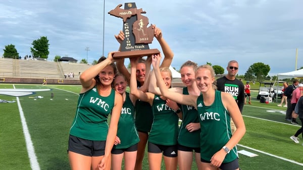 Alumnos de la Western Michigan Christian School celebran con un trofeo en el campo deportivo frente a un estadio.