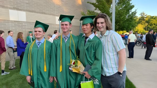 Un grupo de graduados de la Western Michigan Christian School está en togas y birretes verdes frente a un edificio de ladrillo.