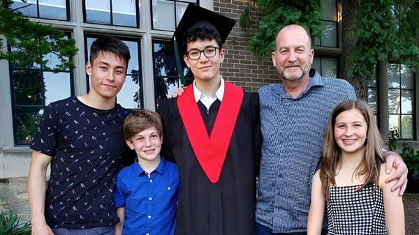 Un grupo de estudiantes de la Western Technical-Commercial School posa frente al edificio de ladrillo con grandes ventanas después de la graduación.